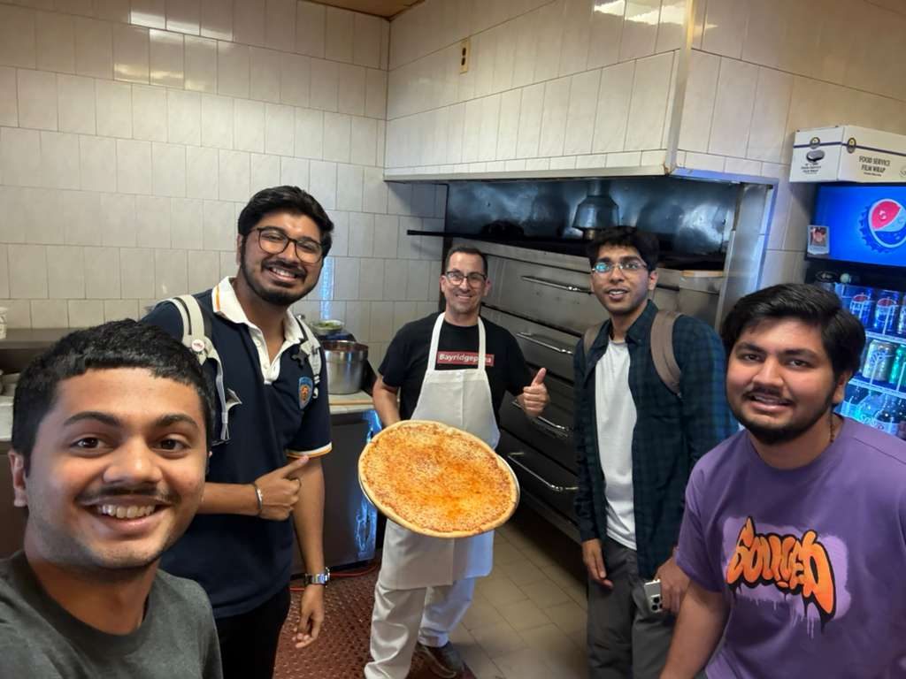 The four of us with the owner in the pizzeria kitchen, in front of the deck oven, holding a pizza he has just taken out.